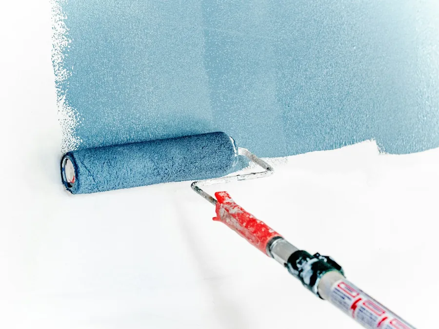 Paint roller rolling blue paint onto a white wall